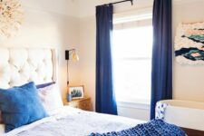 a bold bedroom with a white bed, navy and white bedding, navy curtains, a macrame artwork and a crib
