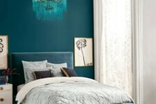 a bold teal wall for a statement and a dusty blue upholstered bed plus a matching ottoman