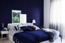 a bright bedroom with a navy accent wall, a white bed with printed blue bedding, simple nightstands and a fluffy pendant lamp