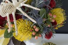 a bright floral arrangement with mustard, red blooms, berries and thistles plus a large spider on top