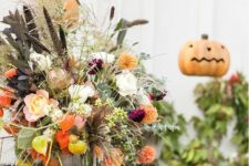 a bright rustic Halloween centerpiece with fresh peachy, orange and dried blooms, dark and usual foliage and greenery