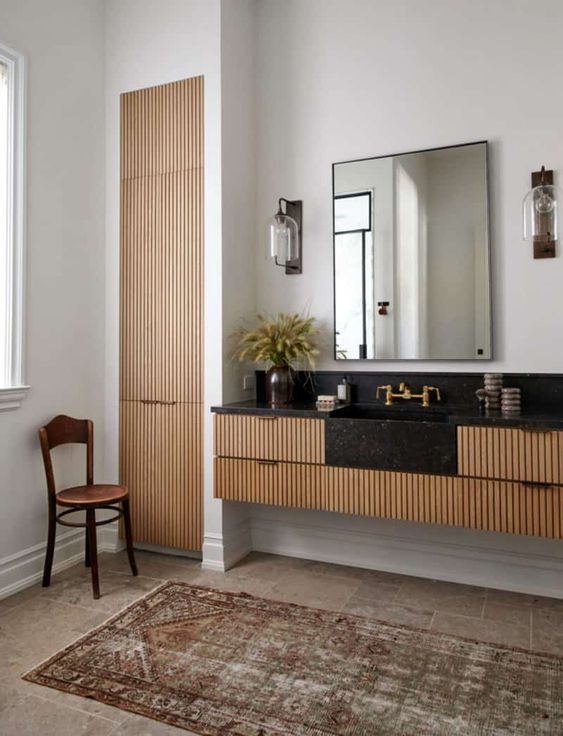 A built in fluted vanity with an elegant black stone countertop, a mirror, sconces and a matching fluted built in wardrobe