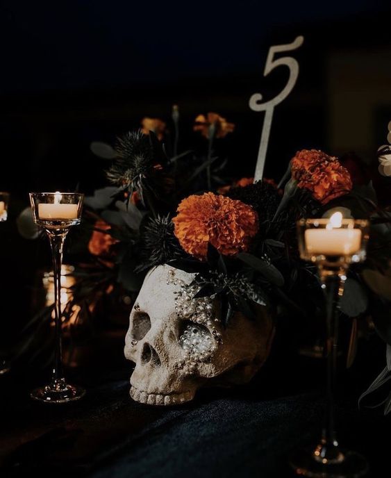 a catchy Halloween decoration of a pearl skull with dark blooms and bold orange marigolds is a bold centerpiece