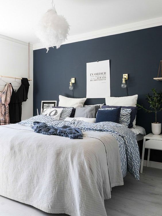 a catchy modern bedroom with a midnight blue accent wall, a bed with navy and white bedding, white nightstands and a fluffy pendant lamp