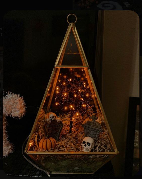 A chic Halloween terrarium with moss, tombstones and skulls, jack o lanterns and a lit up tree is a cool idea