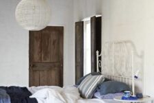 a chic bedroom with shabby chic wooden beams, a forged bed with indigo and white bedding, a nightstand and a rug
