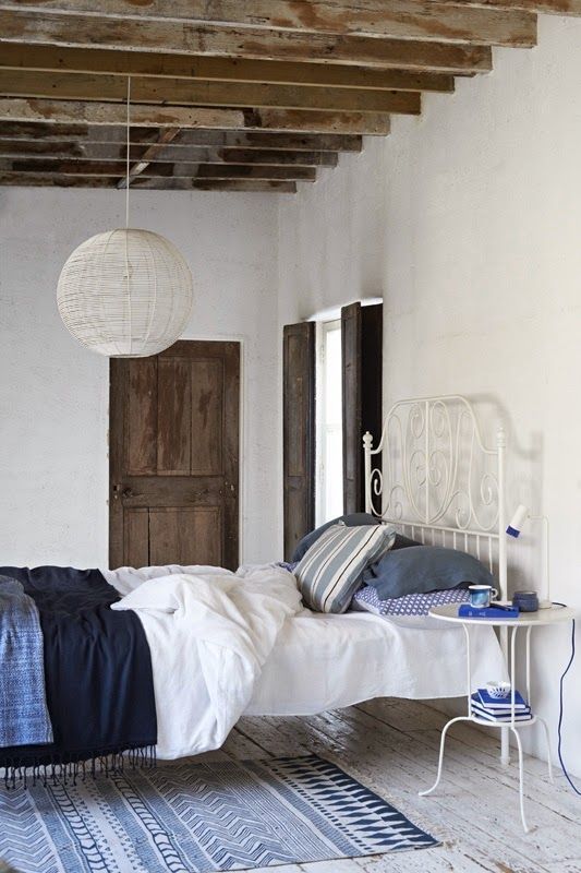 a chic bedroom with shabby chic wooden beams, a forged bed with indigo and white bedding, a nightstand and a rug