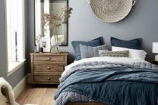 a chic blue bedroom with stained wooden furniture, a woven basket on the wall, blue bedding, a mirror, a boho rug and some faux fur