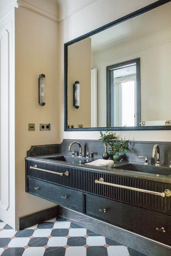 a chic built-in black vanity with a sleek and fluted part, a black counterrop, brass fixtures, a mirror in a black frame