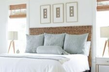 a chic coastal bedroom with a blue bed with a wicker headboard, a rattan bench, a wall gallery with seashells and a vintage chandelier