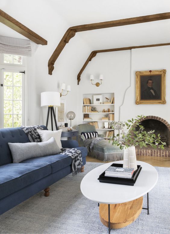 A chic modern living room with an arched fireplace, built in shelves, a navy sofa, a grey daybed and a tiered coffee table
