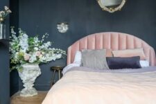 a chic moody bedroom with soot walls and a chest for storage, a light pink bed, refined lighting and blooms