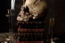 a cloche with a stack of books, a skull and snails is a scary and creative Halloween decor idea