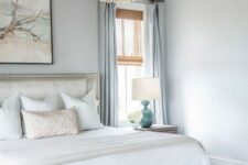 a coastal bedroom in light and pastel blues, with a chic bed and bench, a wood bead chandelier, blue textiles and an artwork