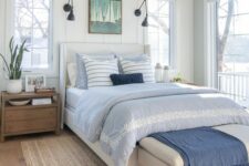 a coastal bedroom with shiplap walls, a white bed with blue and white bedding, a white bench with a blue blanket and a seagrass rug