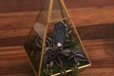 a cool mini Halloween terrarium with moss, faux greenery and leaves, skulls, a tombstone and pebbles