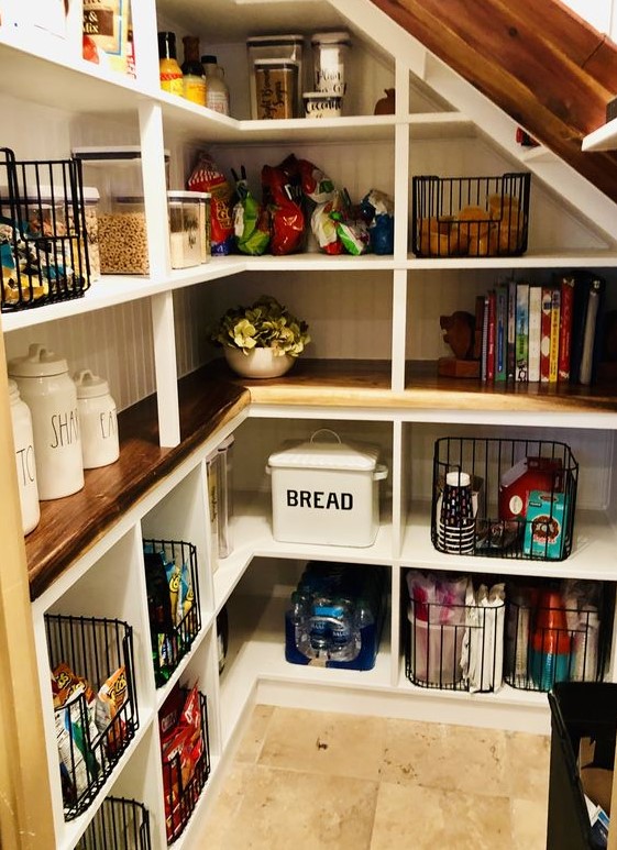 A cozy and cute farmhouse under stairs pantry with shiplap, built in shelves, stained countertops, wire baskets, glass and porcelain storage units