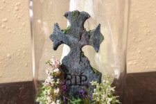 a creative Halloween cloche with hay, blooms, a tombstone and a ghost is a cool decoration to rock