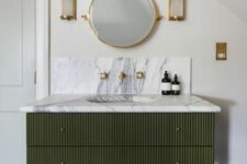a dark green fluted vanity with an additional shelf, a white marble countertop, a round mirror and fluted sconces