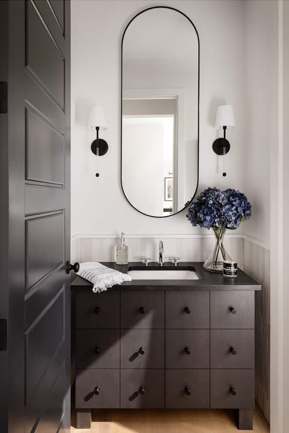 A dark stained bathroom vanity with multiple drawers, an oval mirror and sconces is a cool idea to add a refined touch to the space