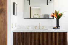 a dark-stained fluted vanity with a stone countertop, a mirror in a black frame, black pendant lamps and bold blooms