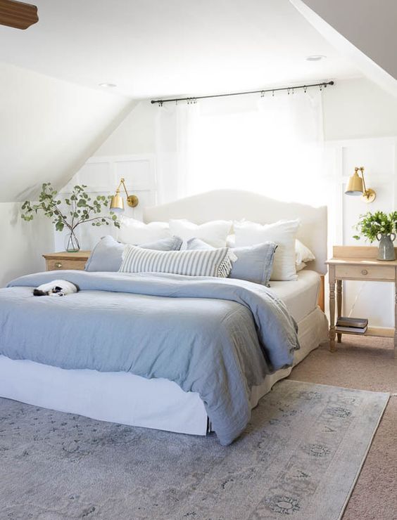 A delicate attic bedroom with a white bed and blue bedding, light stained nightstands and greenery