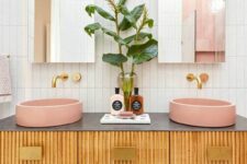 a fluted floating double vanity with pink vessel sinks, greenery, gold geo knobs and fixutres and arched mirrors