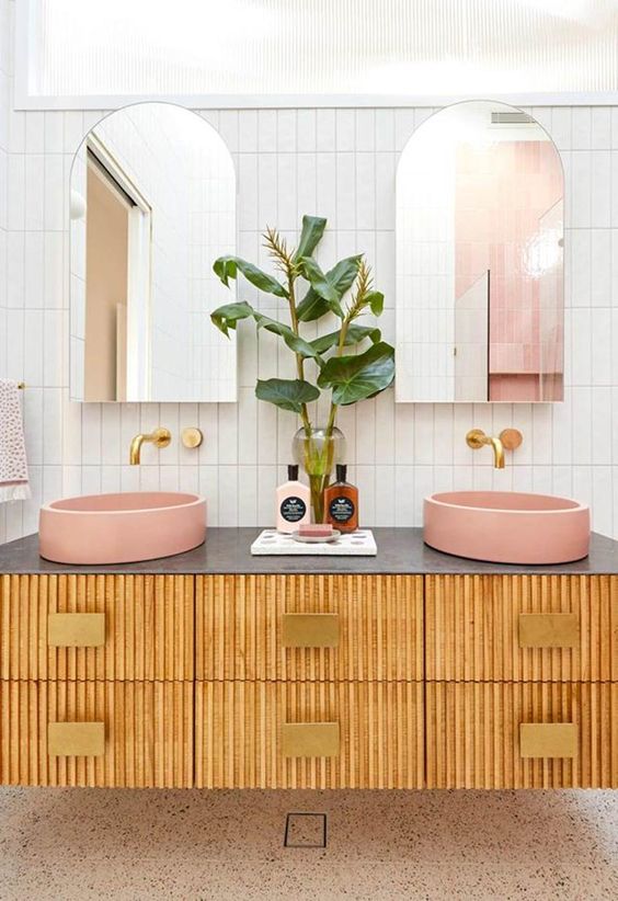 a fluted floating double vanity with pink vessel sinks, greenery, gold geo knobs and fixutres and arched mirrors