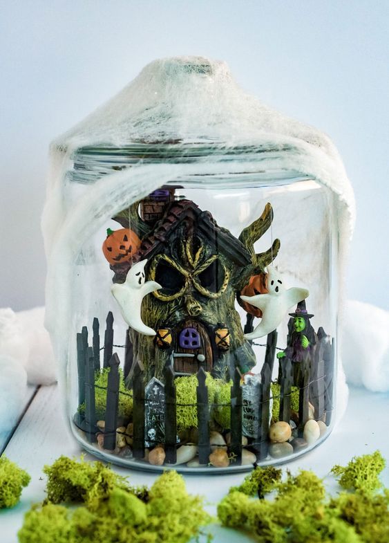 a fun Halloween terrarium with a mini funky graveyard, a witch, some ghosts, jack-o-lanterns and pebbles