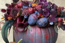 a jaw-dropping grey pumpkin decorated with dark burgundy and purple blooms, plums, berries and apples and dried grasses