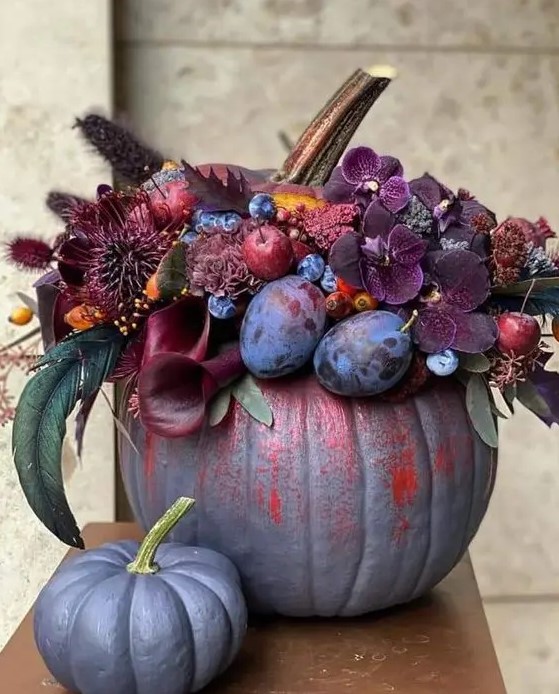 A jaw dropping grey pumpkin decorated with dark burgundy and purple blooms, plums, berries and apples and dried grasses