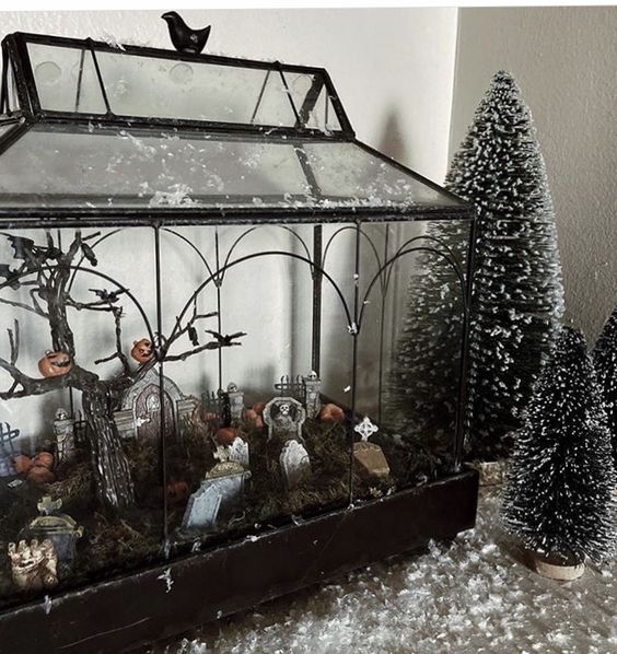 A large Halloween terrarium, a cemetarrium with a tree with jack o lanterns, tombstones, moss is a cool and bold decoration