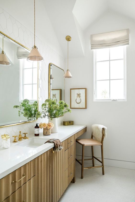 a large fluted vanity with a sink and an additional space for makeup, with mirrors in gold frames and gold fixtures is chic