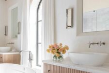 a large refined bathroom with a stained fluted vanity and a vessel sink, a bathtub, mirrors, sconces and wooden beams on the ceiling