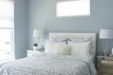 a light blue bedroom with windows, a white bed with blue and white bedding, mirror nightstands and table lamps