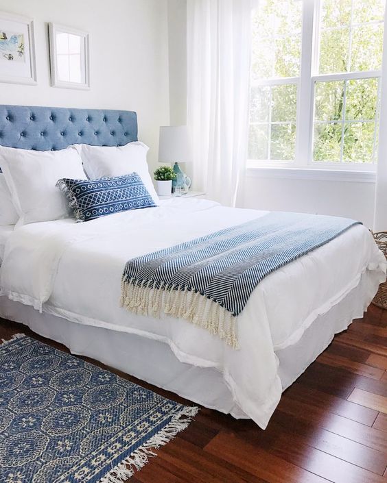 A light filled bedroom with a blue bed, blue and white bedding, a printed rug, a mini gallery wall