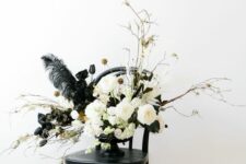 a lovely Halloween flower arrangement with white and black blooms, gilded leaves, seed pods, feathers and some twigs