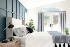 a lovely bedroom with a blue paneled wall, a grey bed with blue and white bedding, stained nightstands and black touches