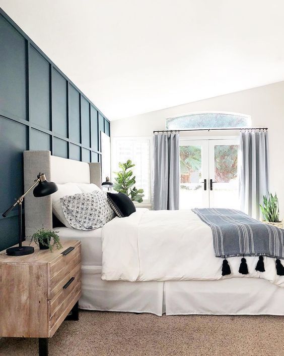 a lovely bedroom with a blue paneled wall, a grey bed with blue and white bedding, stained nightstands and black touches
