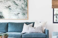 a lovely modern coastal living room with a blue sofa, a light blue chair, a marble top table, a coastal artwork and a neutral rug