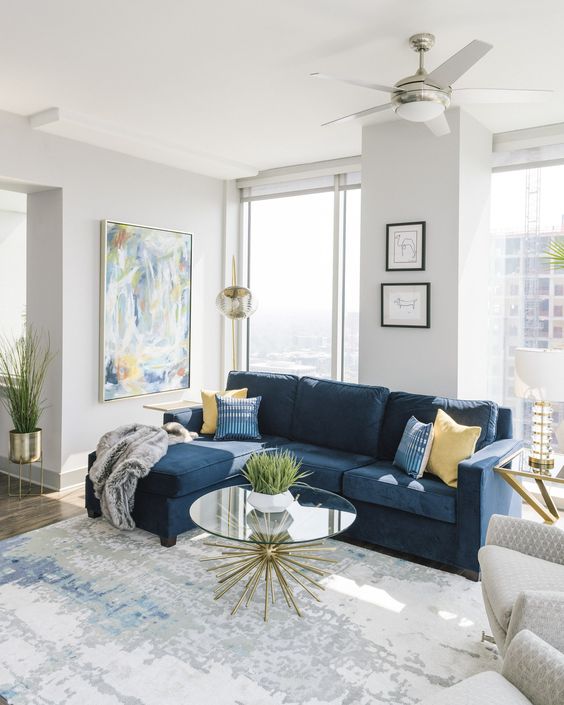 a lovely modern living room with a navy sectional and printed pillows, a printed rug, an abstract artwork and neutral chairs