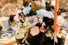 a lovely pastel Halloween arrangement of lilac, blue and pink roses, gilded fronds and leaves plus black touches