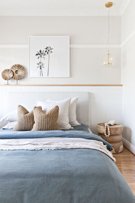 a minimal beach bedroom with a shiplap headboard, a grey bed with blue and white bedding, a wooden nightstand and a pendant lamp