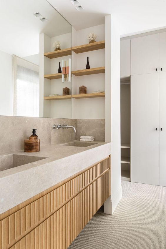 a minimalist neutral bathroom with a light-stained fluted vanity with a slab countertop, niche shelves and a large mirror