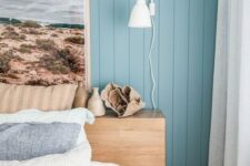 a modern beach bedroom with blue walls, a wooden bed, a statement artwork and printed and blue bedding