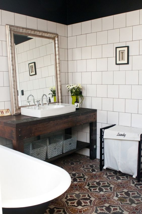 A modern boho bathroom with a dark stained vanity and a sink, a black clawfoot tub and a printed tile floor