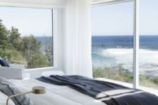 a modern coastal bedroom with glazed walls and a balcony, with white furniture and darker textiles in coastal colors
