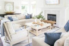 a modern coastal living room with a built-in fireplace, a coffee table, neutral seating furniture, blue pillows, a printed rug