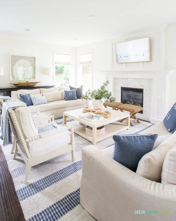 A modern coastal living room with a built in fireplace, a coffee table, neutral seating furniture, blue pillows, a printed rug