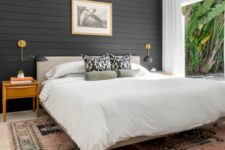 a modern farmhouse bedroom with a black shiplap accent wall, a neutral bed, a printed rug, light-stained nightstands and a cool chandelier